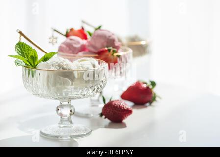 Elegante Komposition mit drei Glas-Dessertschalen mit goldenen Rändern, gefüllt mit Vanilleeis und Erdbeereis. Stockfoto