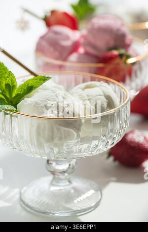 Elegante Komposition mit drei Glas-Dessertschalen mit goldenen Rändern, gefüllt mit Vanilleeis und Erdbeereis. Stockfoto