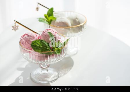 Elegante Komposition mit zwei Dessertschalen aus Glas mit goldenen Rändern, gefüllt mit Vanilleeis und Erdbeereis. Stockfoto
