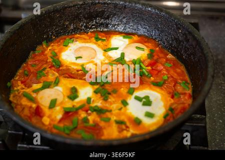 Shakshuka oder Spiegeleier mit Tomaten und grünen Kräutern in einer gusseisernen Pfanne. Leckeres Frühstück, hausgemachte Speisen, gesunde Mahlzeiten. Stockfoto