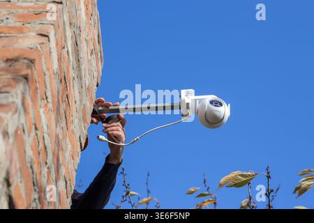 Eine weiße CCTV-Kamera, die auf einer Metallhalterung an einer Ziegelwand montiert ist. Sicherheitssystem, Außeninstallation, Technologie Stockfoto