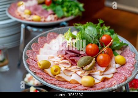 Verschiedene Fleischplatten mit Schinken, Salami, Oliven und Kirschtomaten, die für ein Catering-Buffet oder Bankettservice schön angeordnet sind. Stockfoto