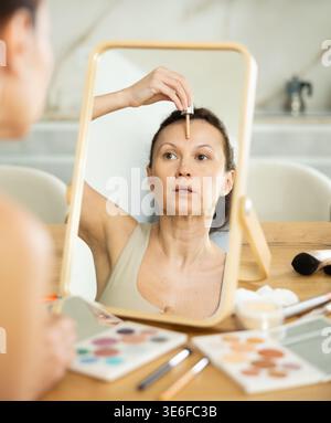Frau, die kosmetische Grundierung auf Gesichtshaut vor dem Spiegel aufträgt Stockfoto