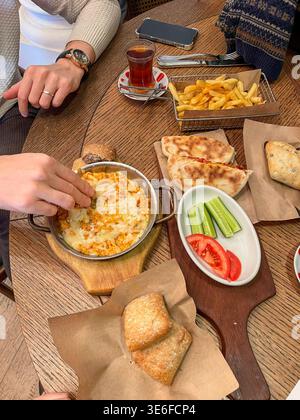 Blick von oben auf Freunde, die sich ein zwangloses Café mit Pommes, Fladenbrot und einem gebackenen Gericht teilen, Tee und Unterhaltung an einem Holztisch genießen. Stockfoto