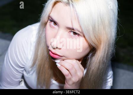 Urban Gen Z Girl mit platinblonden Haaren posiert in trendiger Street-Mode für ein nächtliches Flash-Porträt, auffälliges Make-up und selbstbewusstes Blickkreatin Stockfoto