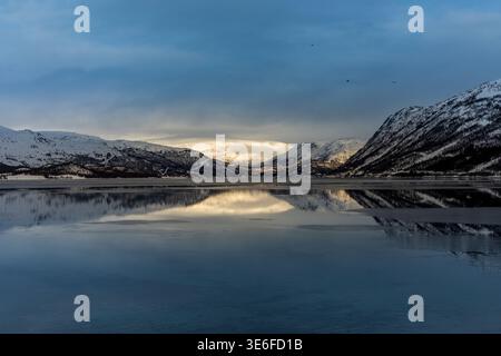 Ruhiger arktischer Fjord in der Nähe von Tromso, Norwegen, mit schneebedeckten Bergen, die sich in der Dämmerung im stillen Wasser spiegeln und die Winterruhe und die Wildnis Lapplands einfangen Stockfoto