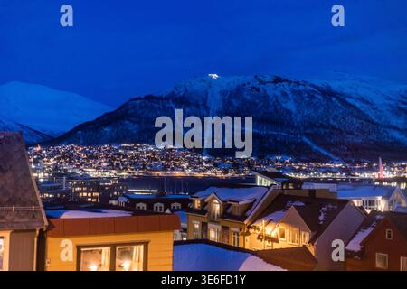Blick über Tromso, Norwegen, mit schneebedeckten Dächern, leuchtenden Lichtern der Stadt und einer dunklen Bergkulisse, die das arktische Lappland atmos einfängt Stockfoto