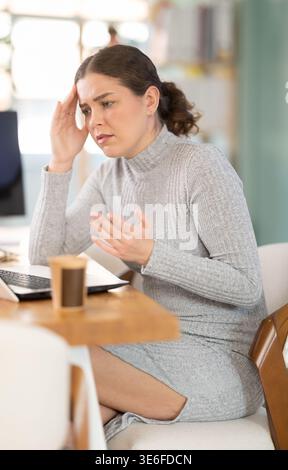 Traurige junge Frau, die im Büro am Laptop arbeitet Stockfoto