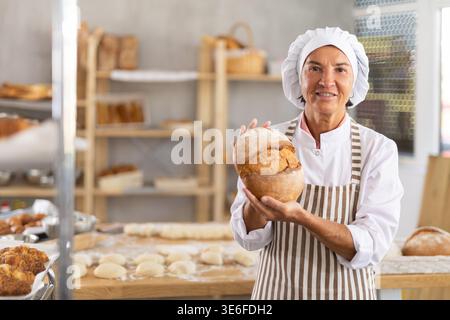 Porträt der fröhlichen älteren Bäckerin mit Brot Stockfoto