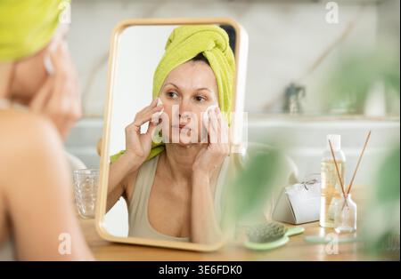 Frau mit handtuchumwickeltem Kopf, Reinigungsgesicht mit Wattepads Stockfoto