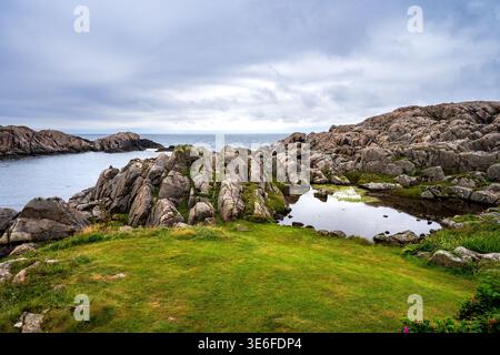 Eindrucksvoller Blick auf die felsige Küste in Lindesnes, Norwegen. Das Foto zeigt einen kleinen Süßwasserteich zwischen zerklüfteten Felsen und grünen Wiesen, mit Stockfoto