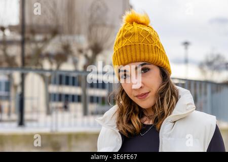 Junge Frau lächelt im Winter mit Senfmütze draußen Stockfoto