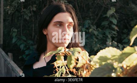 Außenporträt einer jungen Frau in warmem natürlichem Gartenlicht mit Blättern im Vordergrund. Atmosphärisches Lifestyle-Bild mit ruhigem Ausdruck, natura Stockfoto
