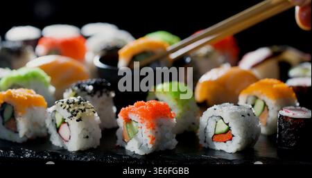 Sushi wird auf einem dunklen Teller serviert, wobei Essstäbchen ein Stück in einem lebhaften Restaurant aufnehmen Stockfoto