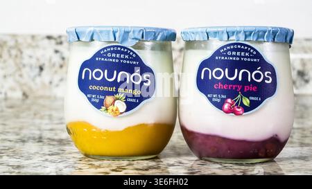 NORWALK, CT, USA - 25. NOVEMBER 2024: Ein Glas griechischer Nounos Joghurt mit Kokosnuss-Mango und Kirschkuchen sitzt auf einer glatten Granitarbeitsfläche Stockfoto