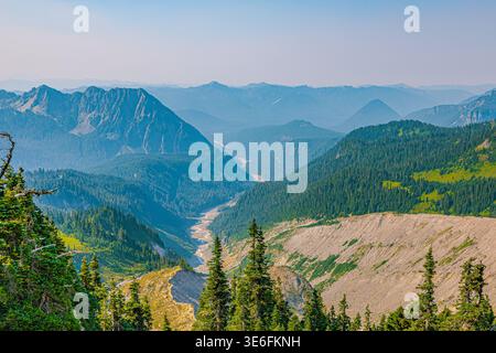 Weitläufiger Blick auf mehrschichtige Bergkämme, ein gewundenes Flusstal und dichte immergrüne Wälder unter einem trüben Himmel. Stockfoto