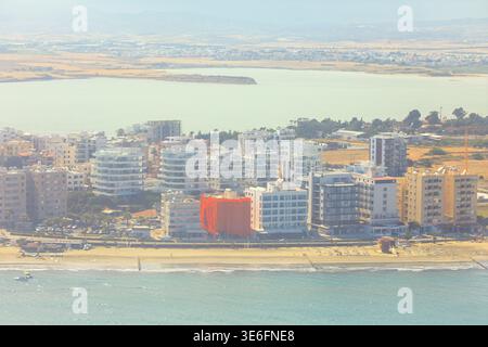 Aus der Vogelperspektive fängt die Küstenstadt von Larnaka, Zypern, ein, wo moderne Gebäude einen Sandstrand säumen. Hinter der Skyline der Stadt liegt das weitläufige Salz Stockfoto