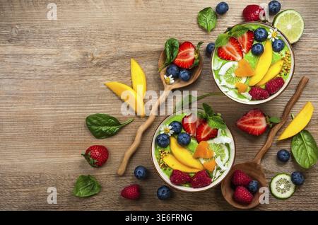 Grüner Smoothie in Schüsseln für gesundes Frühstück. Frischer Bio-Smoothie aus Spinat, Banane, Spirulina, Weizengras und Limette mit Beeren und Obst Stockfoto