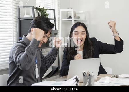 Ein vielseitiges Team von Geschäftspartnern, die ihre Begeisterung zum Ausdruck bringen und ihren Sieg feiern, während sie in einer hellen Büroumgebung an einem Notebook arbeiten Stockfoto