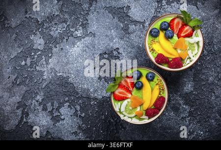 Grüner Smoothie in Schüsseln für gesundes Frühstück. Frischer Bio-Smoothie aus Spinat, Banane, Spirulina, Weizengras und Limette mit Beeren und Obst Stockfoto