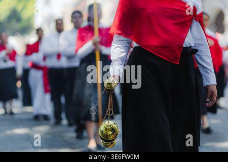 Nahaufnahme einer Frau in rotem umhang und schwarzem Rock, die während der Karfreitagsprozession in Puebla, Mexiko, ein bronzenes Räuchergefäß trug. Stockfoto