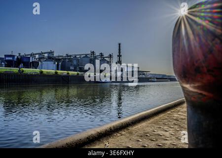 Im Hafen bewegen sich kleine Schiffe auf dem Wasser. Große Industriegebäude sind im Hintergrund zu sehen. Es ist der späte Nachmittag. Hafen Straubing, Lower Stockfoto