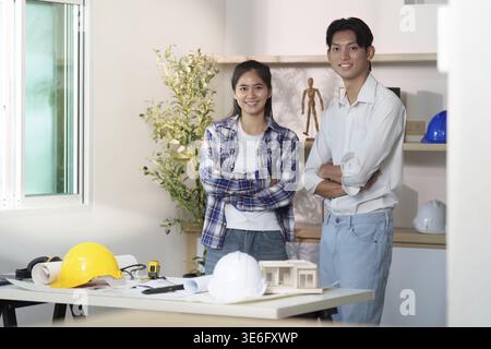 Zwei Ingenieure, die in einem hellen Büro lächeln und gemeinsam an den Entwürfen arbeiten. Konzept von Teamwork und Innovation im Ingenieurwesen Stockfoto
