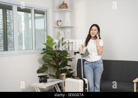Eine junge Frau steht an ihrem Koffer, führt ein Telefongespräch und zeigt die Begeisterung der Reisevorbereitung in einem stilvollen Zuhause Stockfoto
