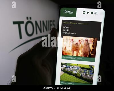 Stuttgart, Deutschland - 08-01-2024: Person mit Mobiltelefon und Website des Fleischverarbeitungsunternehmens Toennies Holding APS Co. KG vor dem Logo. Fokus Stockfoto