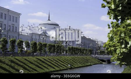Wunderschöne Stadtlandschaft mit einem schmalen Kanal und zwei Hängen, die von grünem Gras auf blauem bewölktem Himmel bedeckt sind. Sommer City Street mit weißen Häusern, und Stockfoto