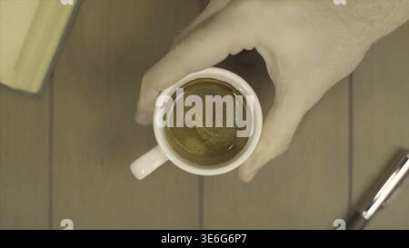 Menschliche Hand Hält Kaffeetasse Morgengetränke. Der Mann bewegt eine Tasse Kaffee. Tasse Kaffee mit fließender Milch auf hölzernem Hintergrund HD Stockfoto
