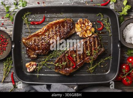 Gegrilltes Striploin-Steak mit Gewürzen und Kräutern auf einer Grillpfanne. Das Strip-Steak, auch New York Strip genannt Stockfoto