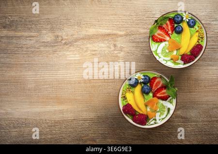 Grüner Smoothie in Schüsseln für gesundes Frühstück. Frischer Bio-Smoothie aus Spinat, Banane, Spirulina, Weizengras und Limette mit Beeren und Obst Stockfoto