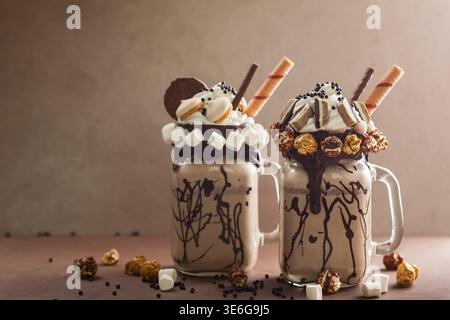 Schokoladenmilchshake mit Eis und Schlagsahne, Marshmallow, süßem Popcorn, Keksen, Waffeln, serviert in glasmauerglas Stockfoto