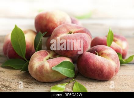 Frische Pfirsiche mit Blättern auf hölzernem Hintergrund. Donut- oder Weinbergtyp von flachem Pfirsich Stockfoto