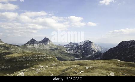 Blick von oben auf das Bergpanorama vor blauem Himmel. Lager. Felsige Berggipfel mit Grasbedeckung am Fuße der Ausläufer schaffen eine wunderschöne Landschaft Stockfoto