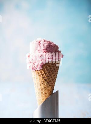 Eis mit Himbeere im Waffelkegel auf blauem Hintergrund Stockfoto