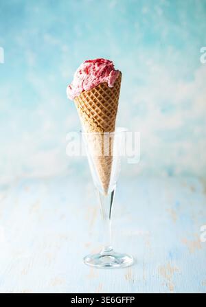 Eis mit Himbeere im Waffelkegel auf blauem Hintergrund Stockfoto