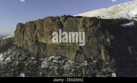 Panoramablick auf Schnee an den Hängen der wunderschönen Winterberge, die von Wald bedeckt sind, an einem sonnigen Tag. Fliegen Sie über atemberaubende Klippen Stockfoto
