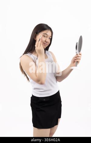 Frau, die in einen Spiegel schaut und Lippenstift im Studio aufträgt Stockfoto