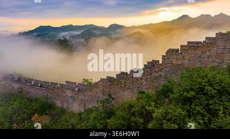 Goldener Sonnenaufgang, der die Chinesische Mauer von Jinshanling über nebeligen Bergkämmen in Nordchina beleuchtet. Stockfoto