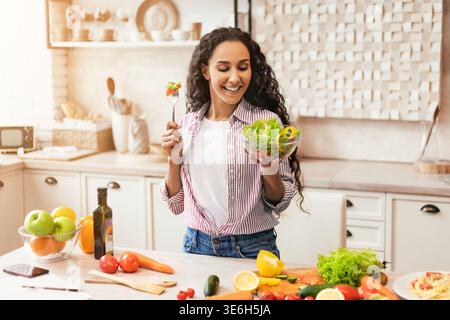 Frau bereitet frischen Salat in der Küche mit buntem Gemüse und Obst bei Tageslicht zu Stockfoto