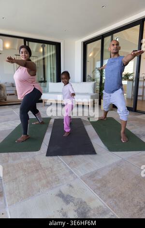 Afroamerikanische Familie in Activewear übt Yoga in gekachelten Sonnenzimmer auf zwei grünen, schwarzen Matten Stockfoto