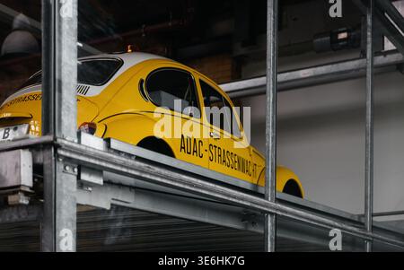 Klassischer ADAC-Pannenhilfe-Käfer im Autoverlader. Ein klassischer gelber VW-Käfer mit ADAC Strassenwacht-Branding, der in einem modernen mechanischen Stapler geparkt ist. Stockfoto