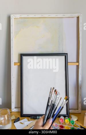 Leere Leinwand mit Pinseln und Farben auf dem Tisch. Kreativer Arbeitsbereich, Einrichtung eines Kunststudios, Konzept für Hobby-Malerei. Stockfoto