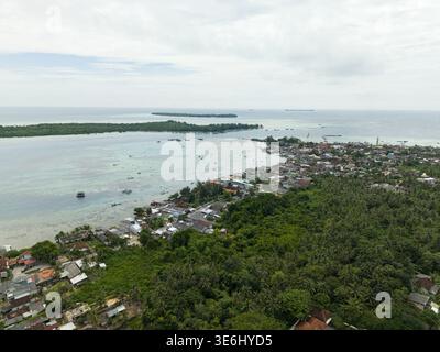 Aus der Vogelperspektive auf eine lebhafte Küstenstadt, wo smaragdgrüne Wälder auf das türkisfarbene Meer treffen, im Kontrast zu den Terrakotta-Dächern Karimunjawa, Central Jav Stockfoto
