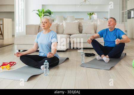 Yoga-Achtsamkeitsmeditation. Älteres erwachsenes Ehepaar, das zu Hause Yoga praktiziert. Die Frau des mittleren Alters sitzt in Lotusposition auf Yogamatte und meditiert entspannend. Familie, die Atemübungen macht Stockfoto