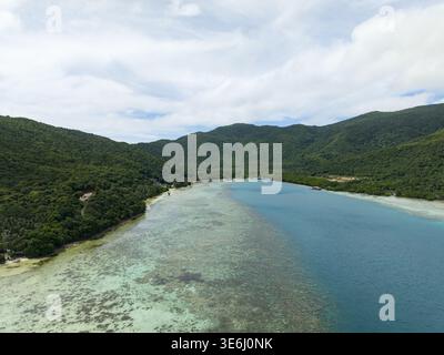 Aus der Vogelperspektive das pulsierende türkisfarbene Wasser trifft auf üppige grüne Hügel, ein ruhiger Zufluchtsort ins Paradies Karimunjawa, Zentral-Java, Indonesien. Stockfoto