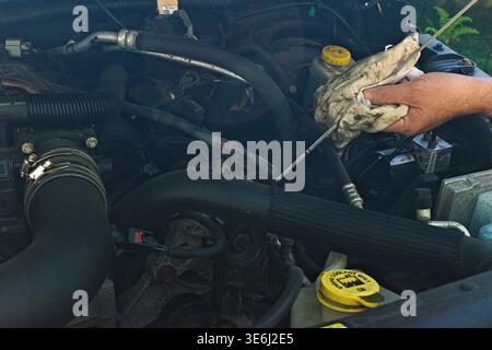 Die Hand einer Person verwendet einen schmutzigen Lappen, um den Ölstand im Motorraum eines Fahrzeugs zu prüfen Stockfoto