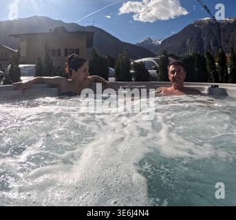 Mann und Frau entspannen sich in einem Whirlpool im Hotelgarten. Hinter ihnen das Profil der Berge. Der Mann und die Frau sind kaukasischer Herkunft Stockfoto